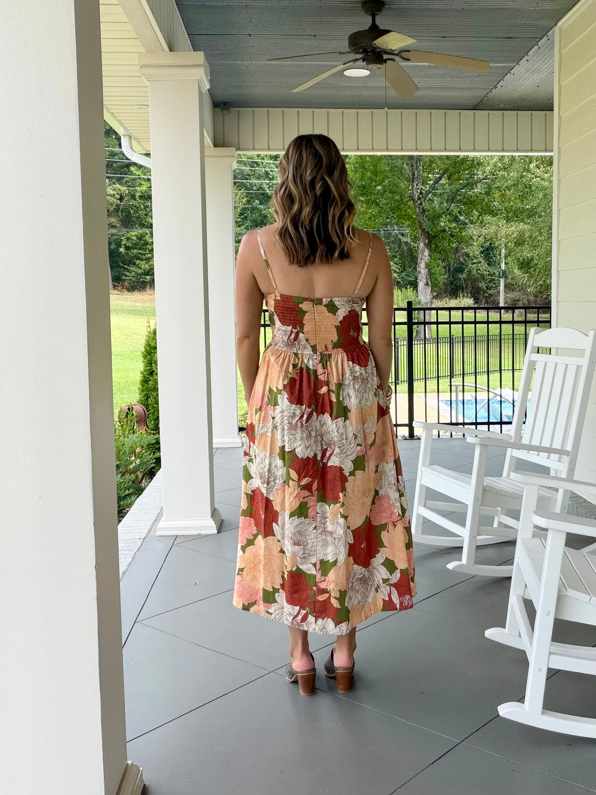 A stunning sleeveless, pleat detail  midi dress with a large floral print in orange, red, cream, and green. 