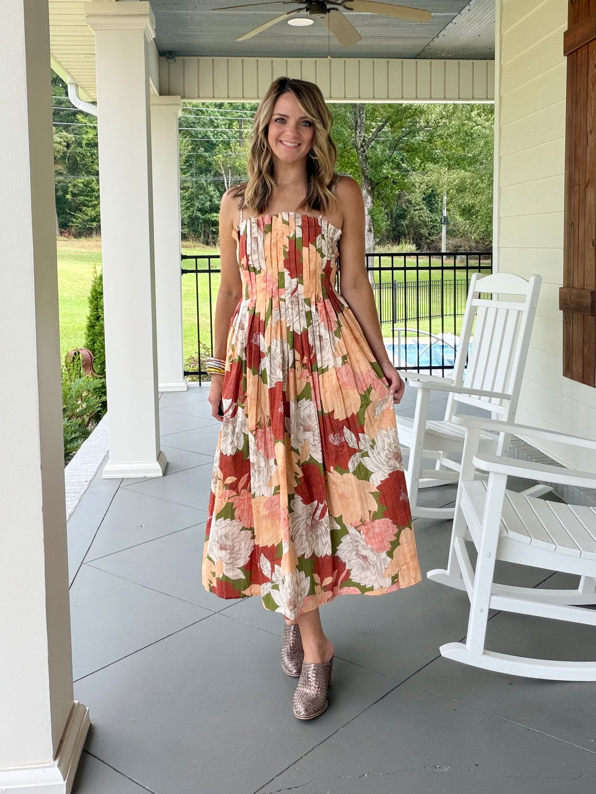 A stunning sleeveless, pleat detail  midi dress with a large floral print in orange, red, cream, and green. 