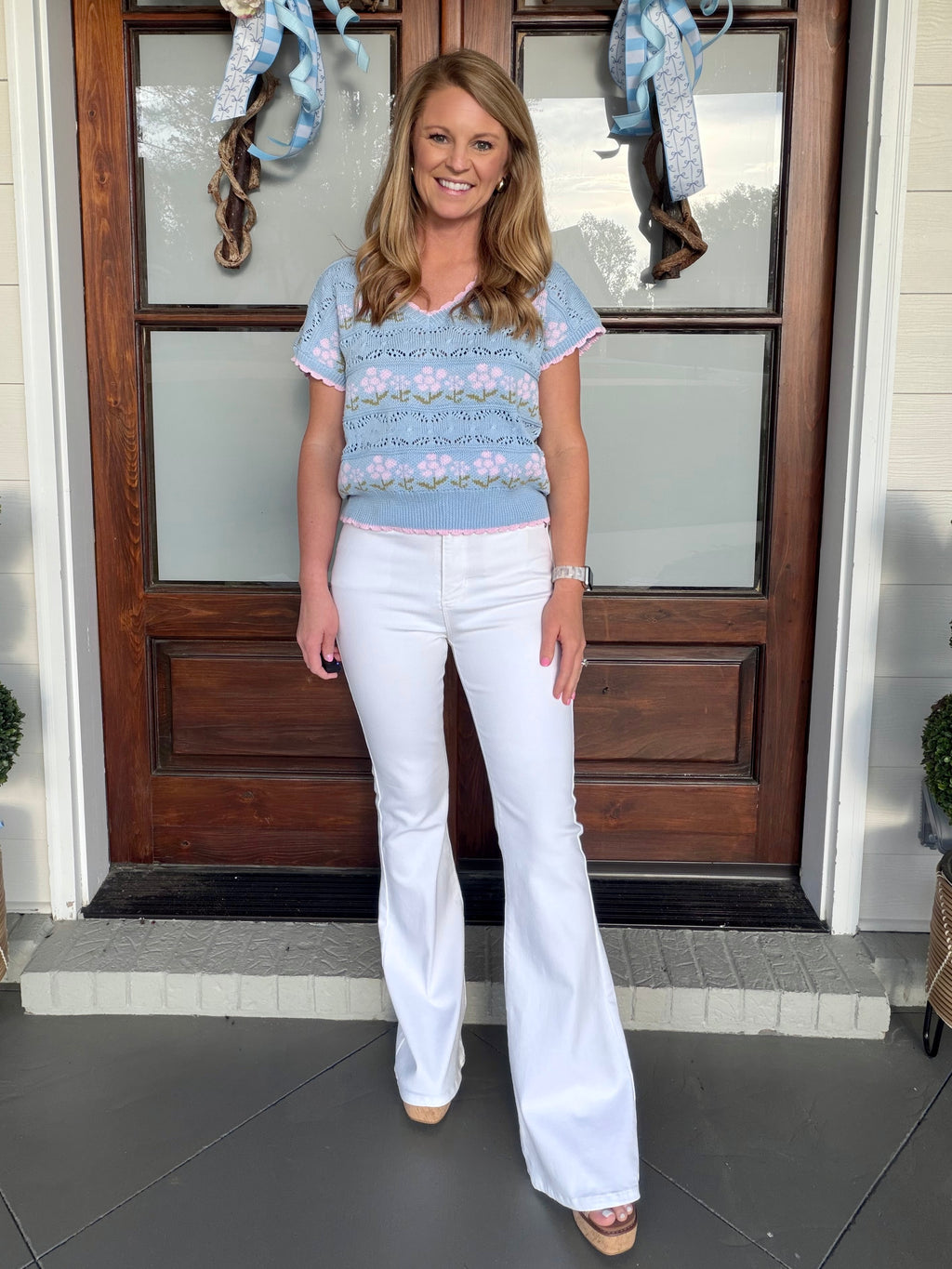front view of white flared jeans styled with a blue floral short-sleeve knit top