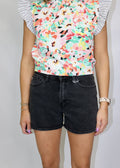 front view of washed black denim shorts with finished hems and a colorful floral top