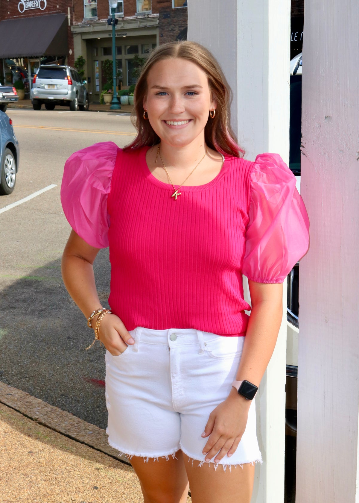 model wearing white raw-hem denim shorts with a bright pink puff-sleeve top outdoors