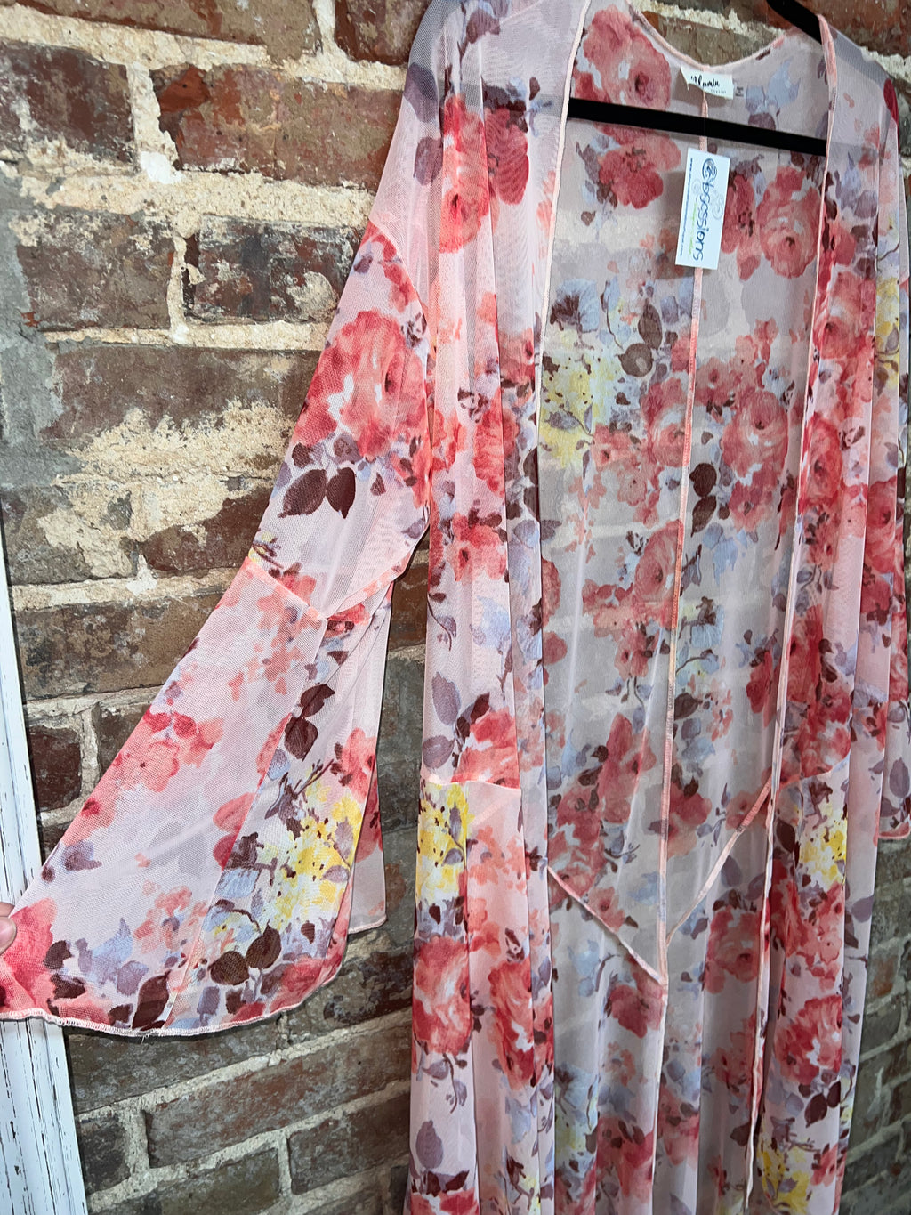 close-up of a sheer pink floral kimono showing its wide sleeve and rose pattern