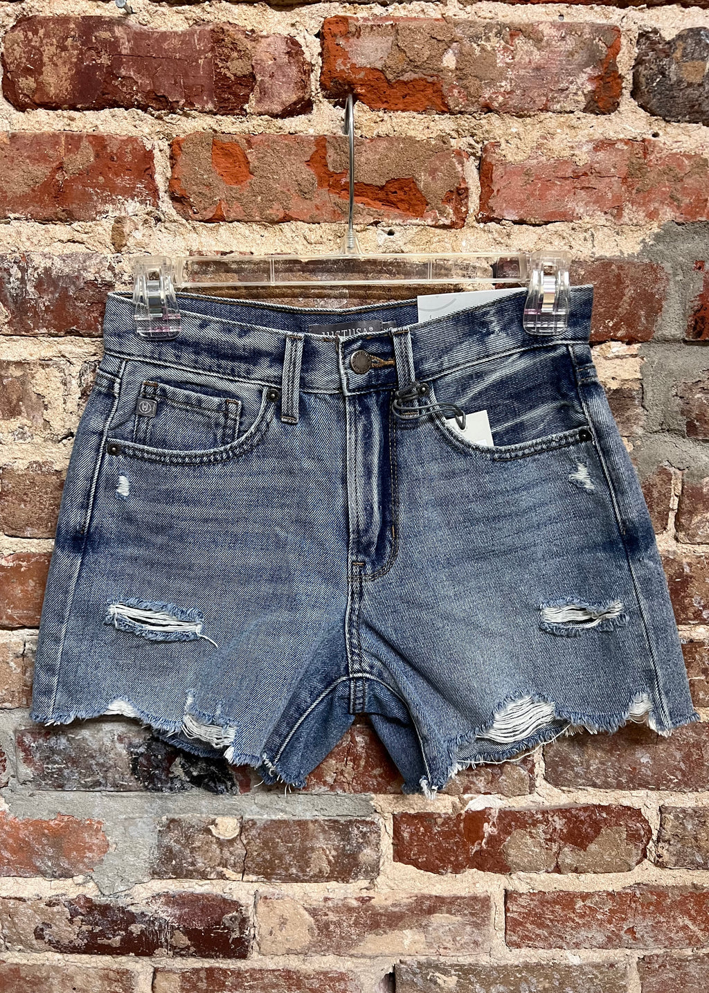 distressed medium-wash denim shorts with raw hems and front pockets on a hanger