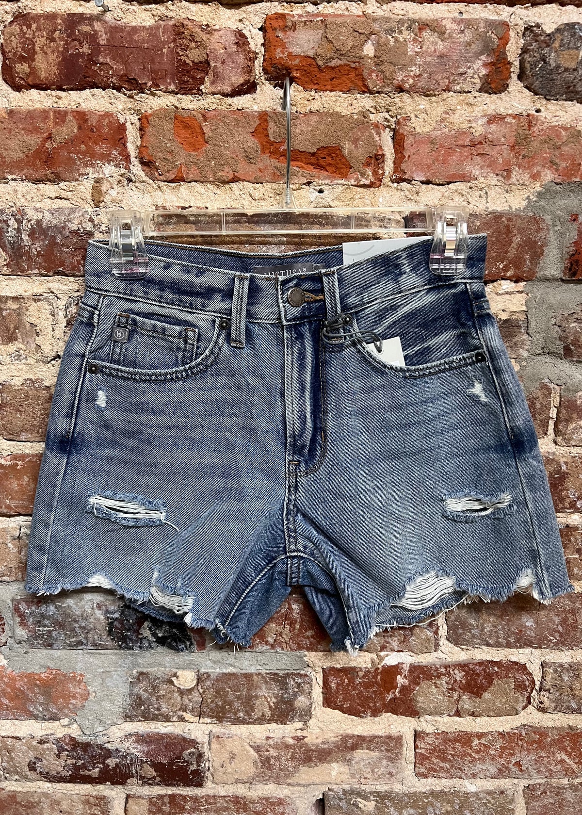 distressed medium-wash denim shorts with raw hems and front pockets on a hanger