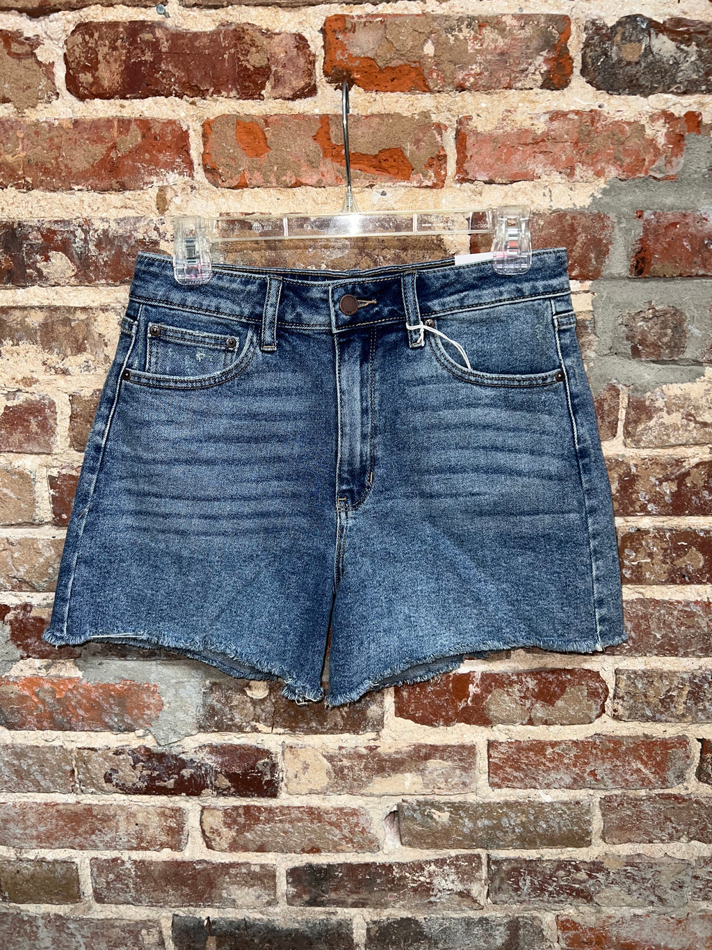 medium-wash denim shorts with a button waist, front pockets and raw hems on a hanger