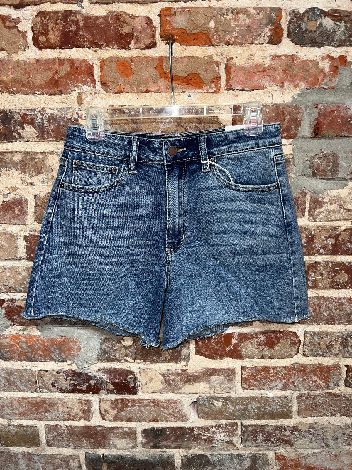 medium-wash denim shorts with a button waist, front pockets and raw hems on a hanger