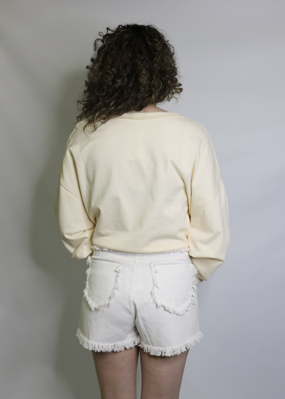 back view of white denim shorts with frayed hems and fringed patch pockets
