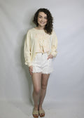 model wearing white fringed denim shorts with a pale yellow graphic sweatshirt