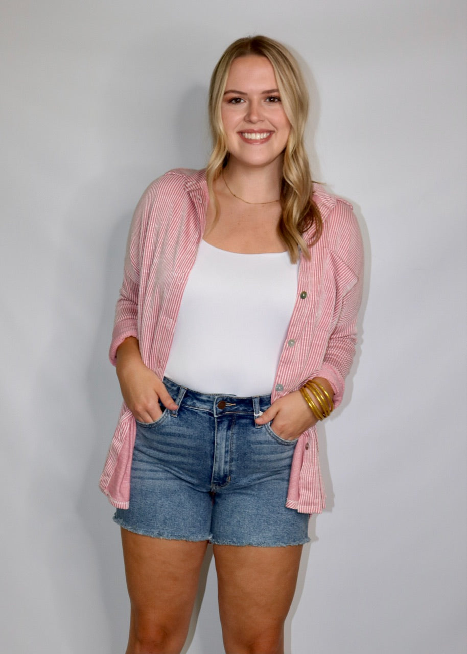 model wearing medium-wash raw-hem denim shorts with a white tank and pink striped shirt