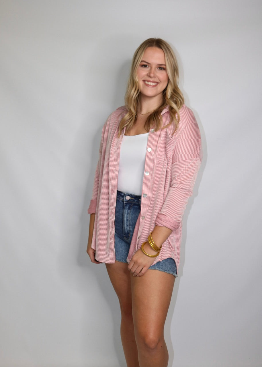 angled view of medium-wash denim shorts styled with a white tank and open pink striped shirt