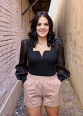 model wearing a black notched-neck top with sheer balloon sleeves and beige cuffed shorts