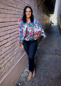 model wearing a teal multicolored abstract-print blouse with tie sleeves and dark jeans