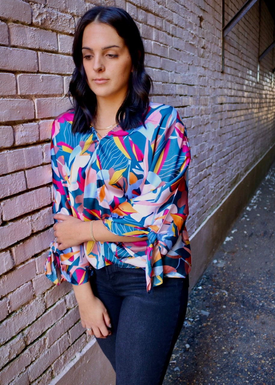 close-up of a teal, pink and yellow abstract-print v-neck blouse with sleeve ties
