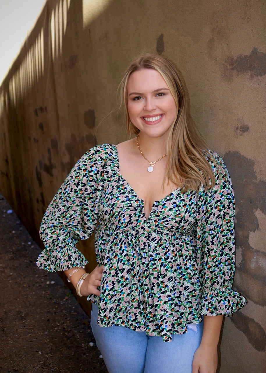model wearing a multicolored printed peplum blouse with a notched neckline and ruffled sleeve cuffs